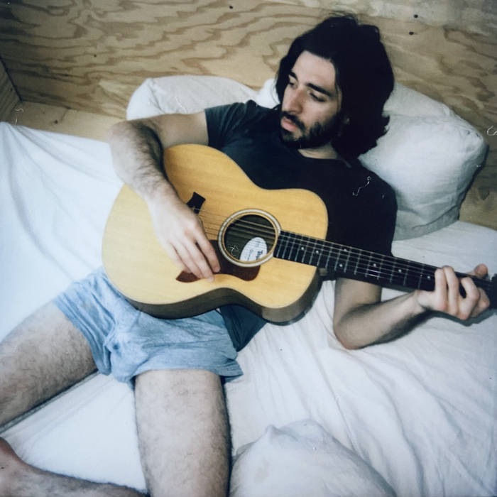 Image of Logan Bowden in a bed with an acoustic guitar